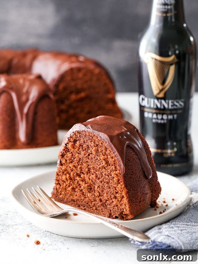 A slice of rich chocolate stout bundt cake with ganache, served on a plate with a fork, ready to be enjoyed.