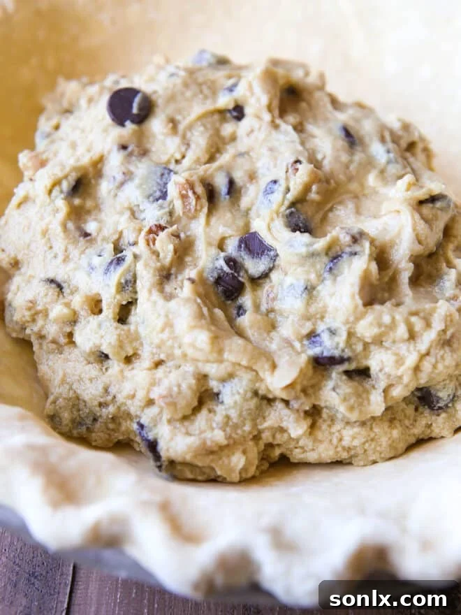 Unbaked cookie dough being carefully spooned into a pie crust, ready for baking.