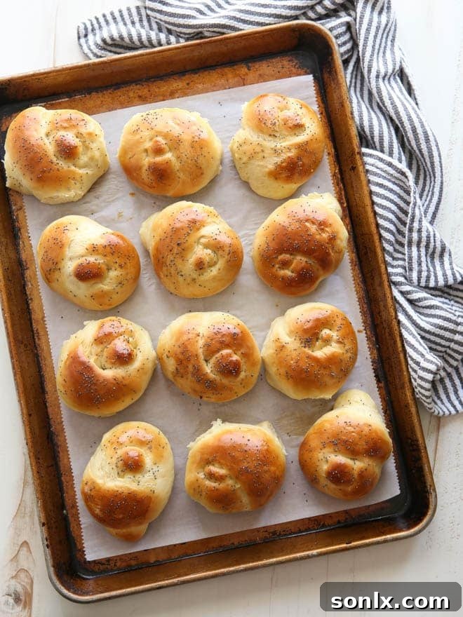 Delicious golden-brown knotted Challah dinner rolls on a baking sheet, ready to be served, highlighting their soft texture and beautiful shape.