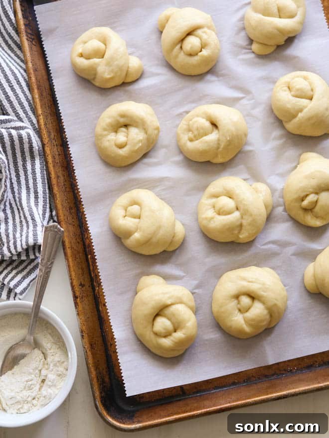 A cluster of beautifully golden knotted dinner rolls arranged on a white serving plate, with a soft focus background, emphasizing their artisanal quality.