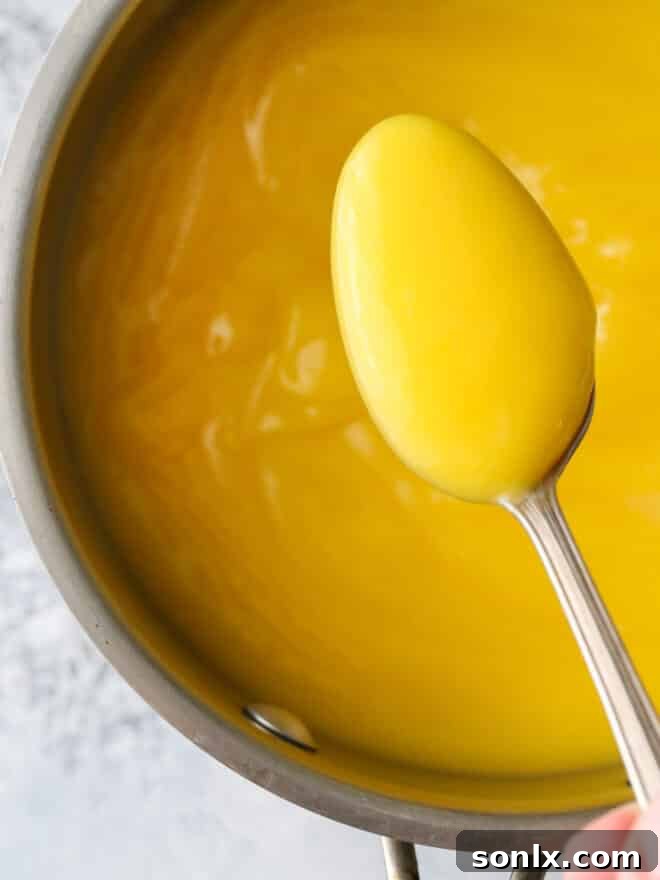 A spoon dipping into a pot of freshly made, glossy lemon curd, showcasing its rich texture.