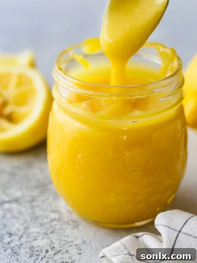 Homemade lemon curd being spooned into a glass jar for storage, highlighting its vibrant color.
