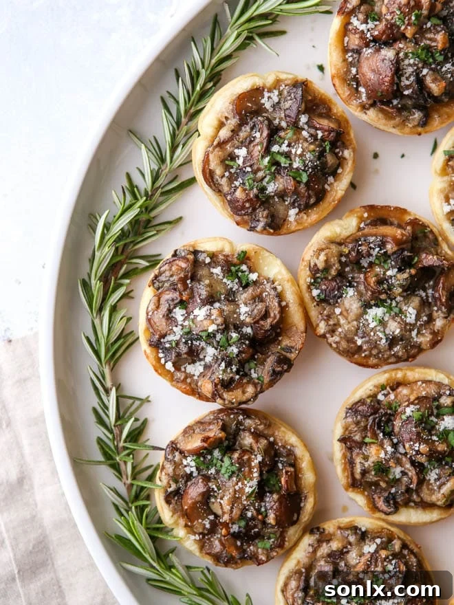 Close-up view of golden-brown mini mushroom puff pastry tarts artfully arranged on a serving platter, highlighting their flaky texture and inviting appearance.