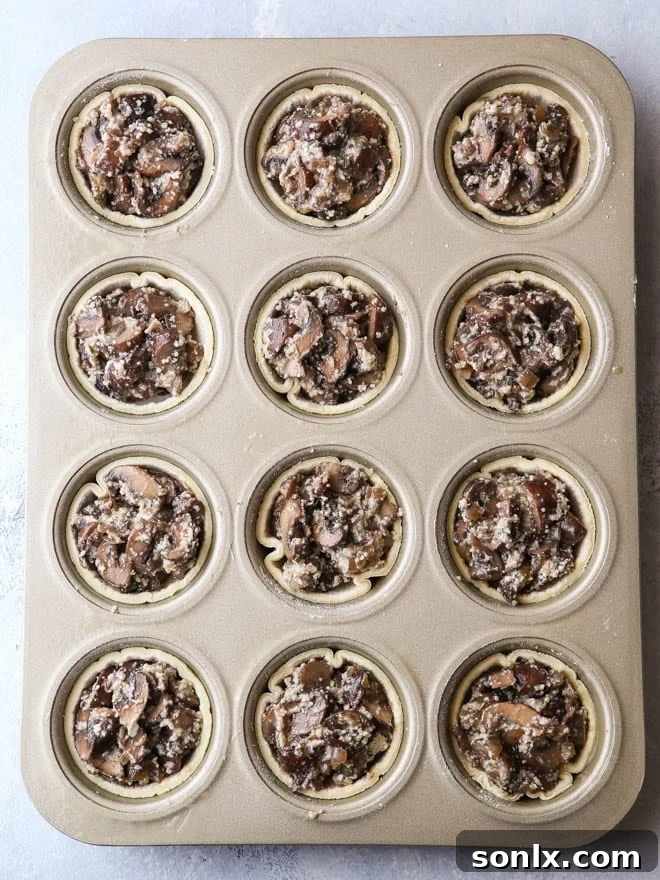 Unbaked mini mushroom tarts, carefully filled with the savory mushroom mixture and pressed into a muffin pan, poised for baking.