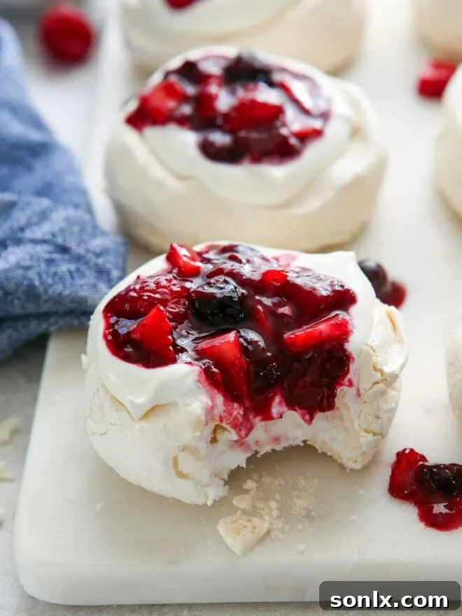 A mini pavlova with a bite taken out, showing layers of whipped cream and berry compote
