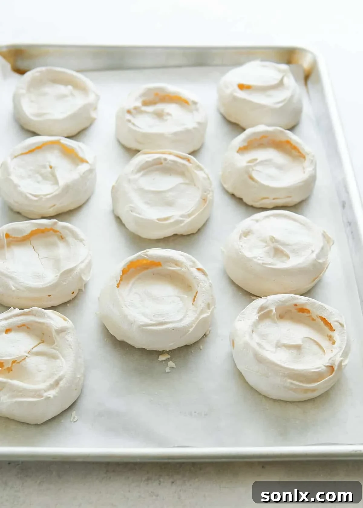 Baked mini pavlovas lined up on a baking sheet, showcasing their crisp exterior
