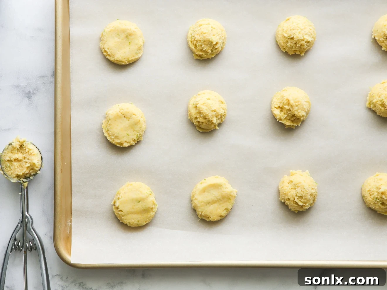 cookie scoop with lime cornmeal cookie dough on a parchment-lined sheet pan, ready for baking